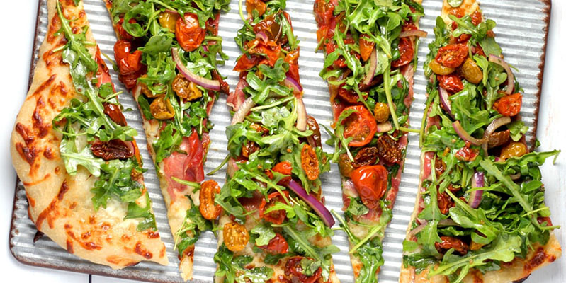 Viele verschiedene Zutaten, wie Rucola, Zwiebeln oder Tomaten, sind zum Belegen einer Pizza beliebt